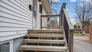 A wooden staircase leading to a house's entrance. - Abby’s Lodge | Modern 2BR Retreat | Prime Downtown Location (Fredericton)