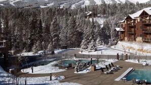Un complex turístic amb zona de piscina, paisatge cobert de neu i muntanyes al fons.