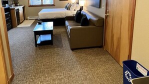 Habitació d'hotel petita amb llit, sofà, taula de cafè, escriptori i cuina americana.