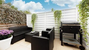 Une terrasse extérieure aménagée avec des meubles en osier, un barbecue et une clôture blanche ornée de plantes grimpantes.