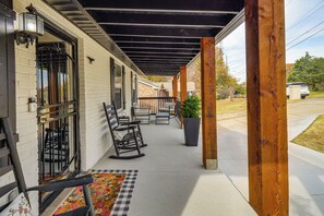 Une véranda couverte avec une balustrade en bois, une chaise berçante et une plante en pot.