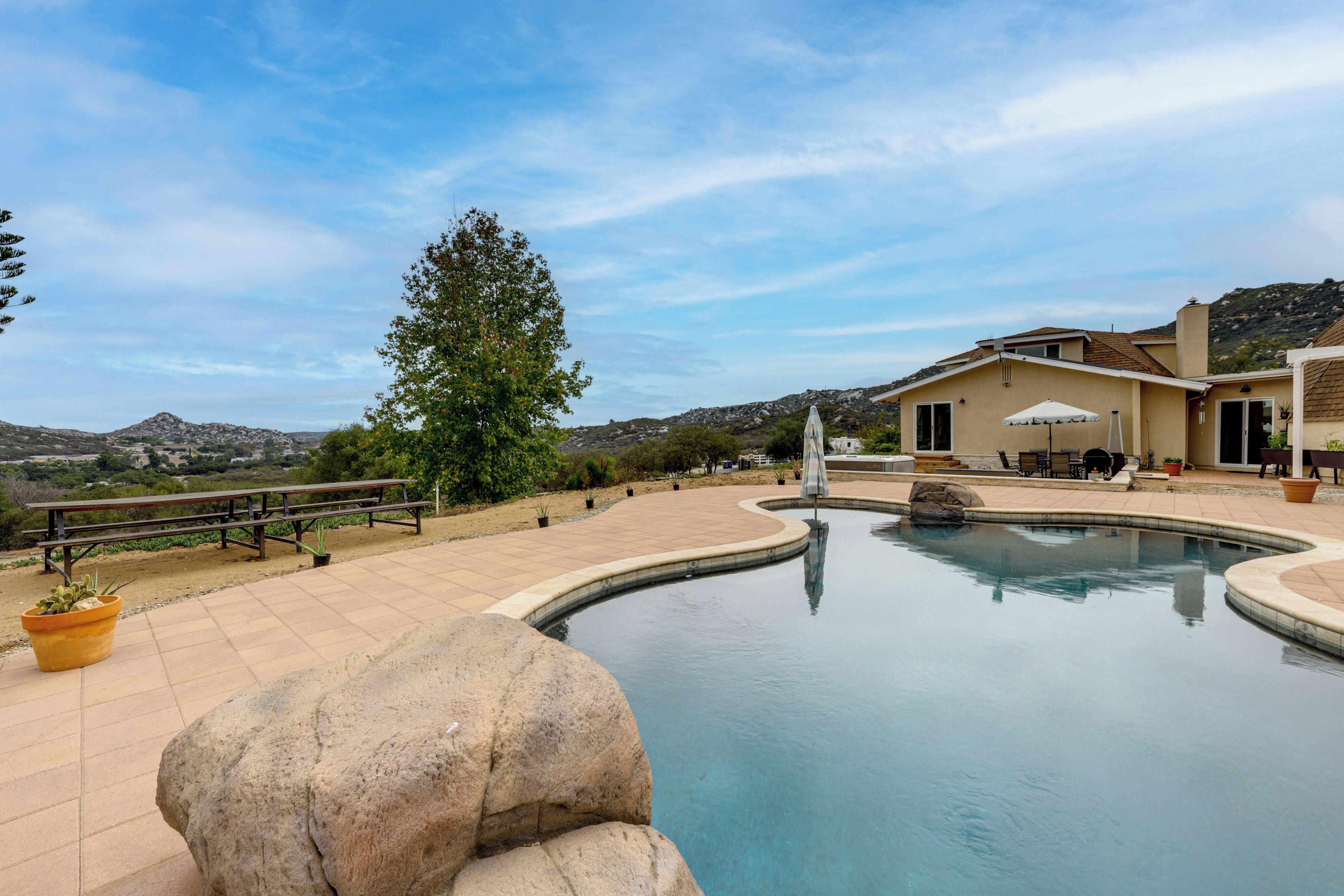 A swimming pool with a curved edge, surrounded by a patio area with outdoor furniture and a large tree.