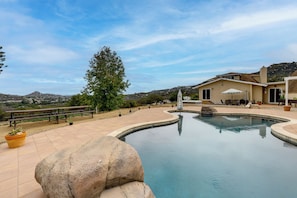 A swimming pool with a curved edge, surrounded by a patio area with outdoor furniture and a large tree. - Near Hiking Trails! Luxe Family Home in Lakeside (Lakeside)