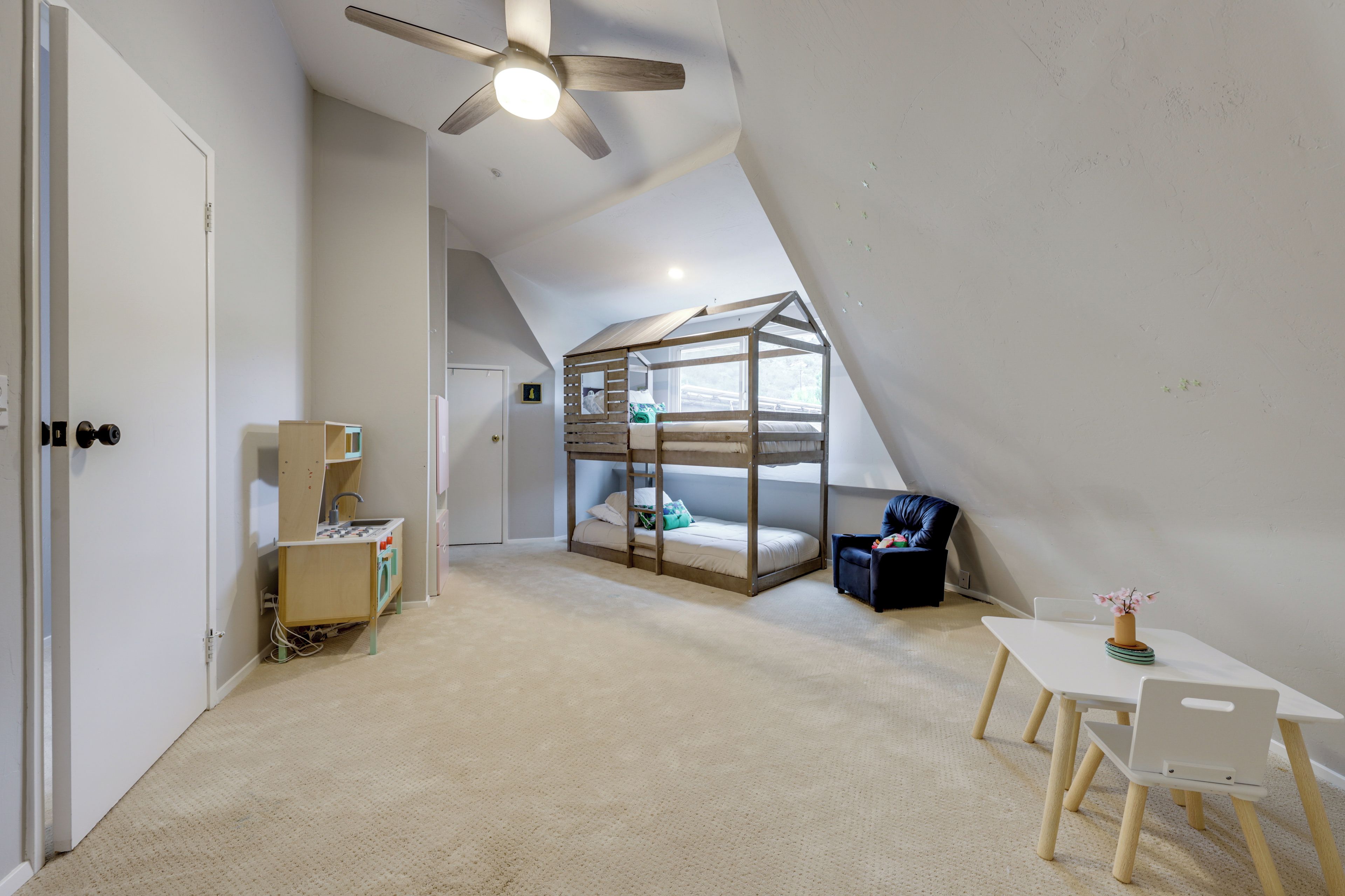 A room with a bunk bed, a desk, a chair, a ceiling fan, and a small table with a vase.