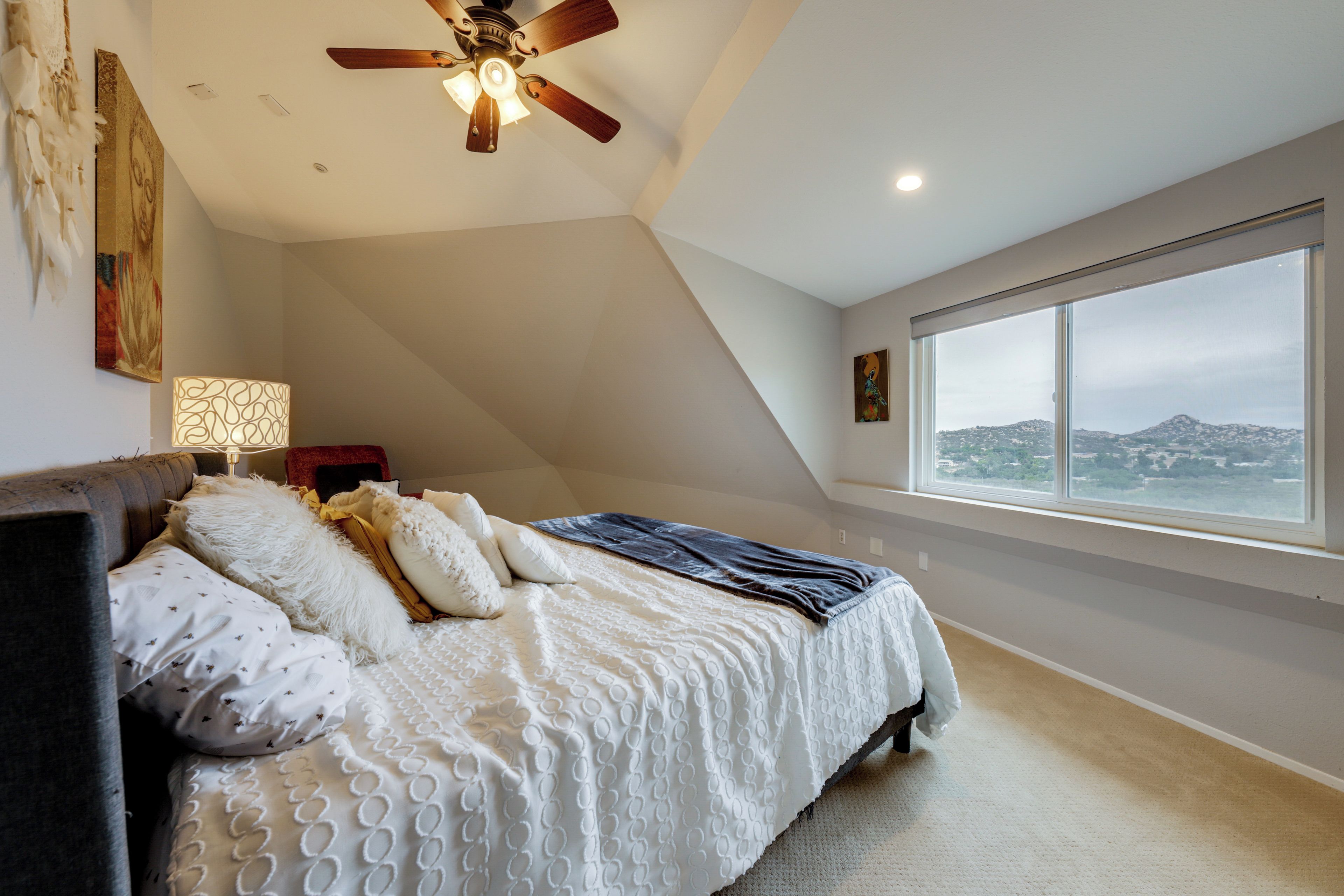 A bedroom with a bed, a ceiling fan, a large window, and a view of a mountain.