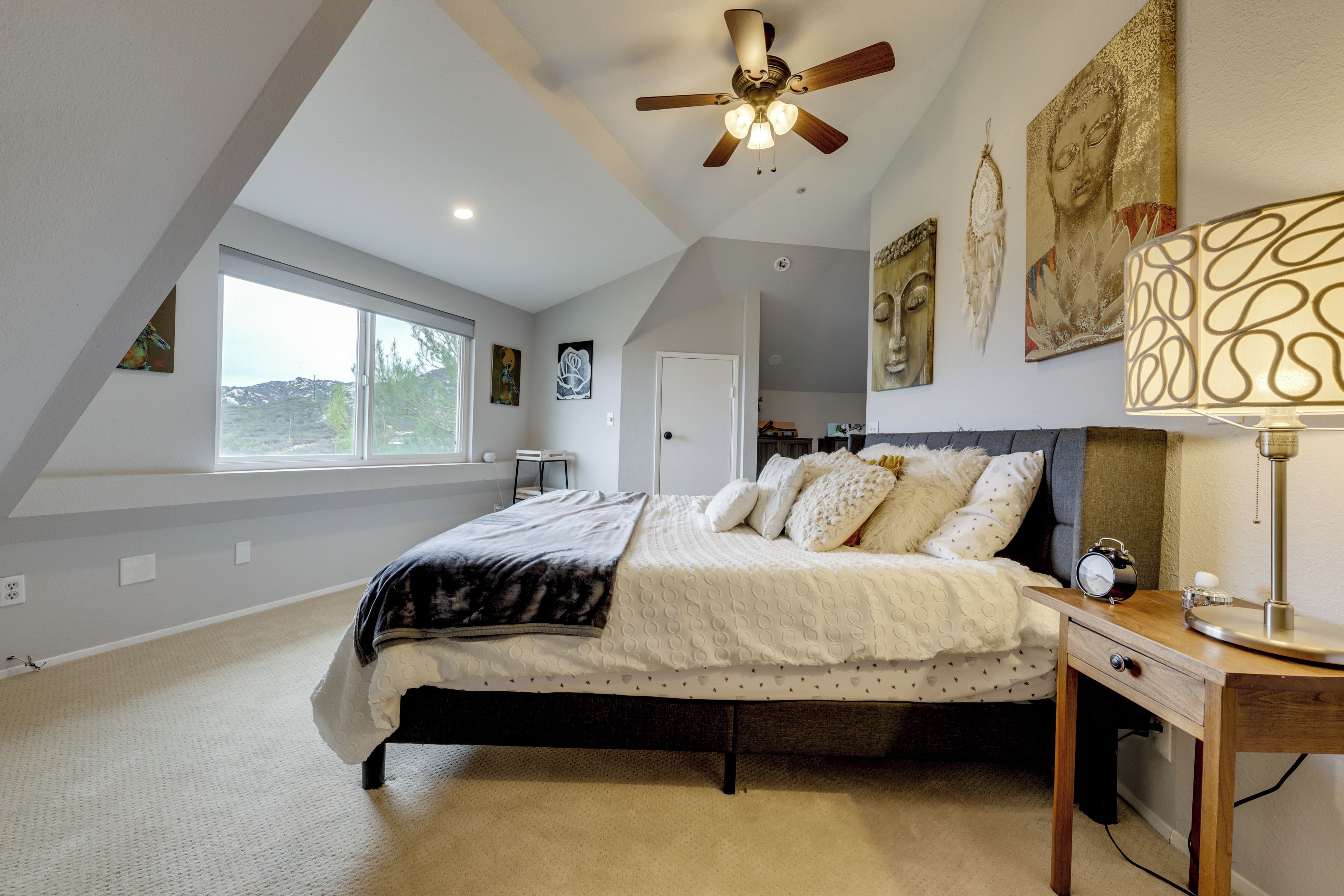 A bedroom with a bed, a ceiling fan, a bedside table, and artwork on the walls.
