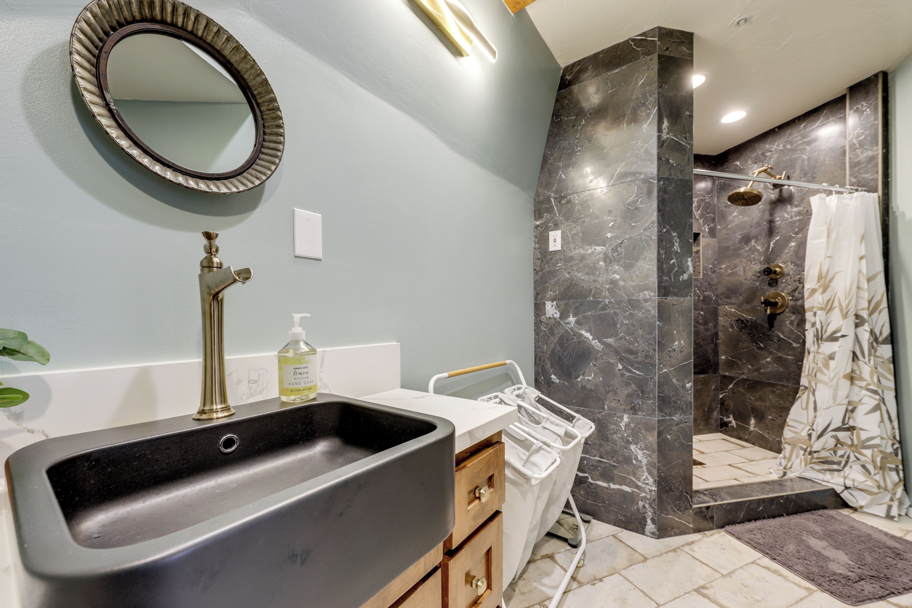 A bathroom with a black sink, a mirror, a shower with a marble wall, and a towel rack.