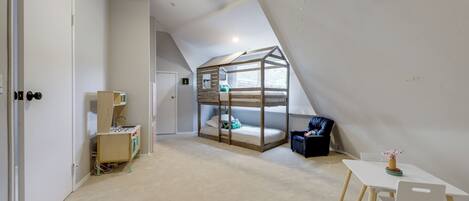 A room with a bunk bed, a desk, a chair, a ceiling fan, and a small table with a vase.