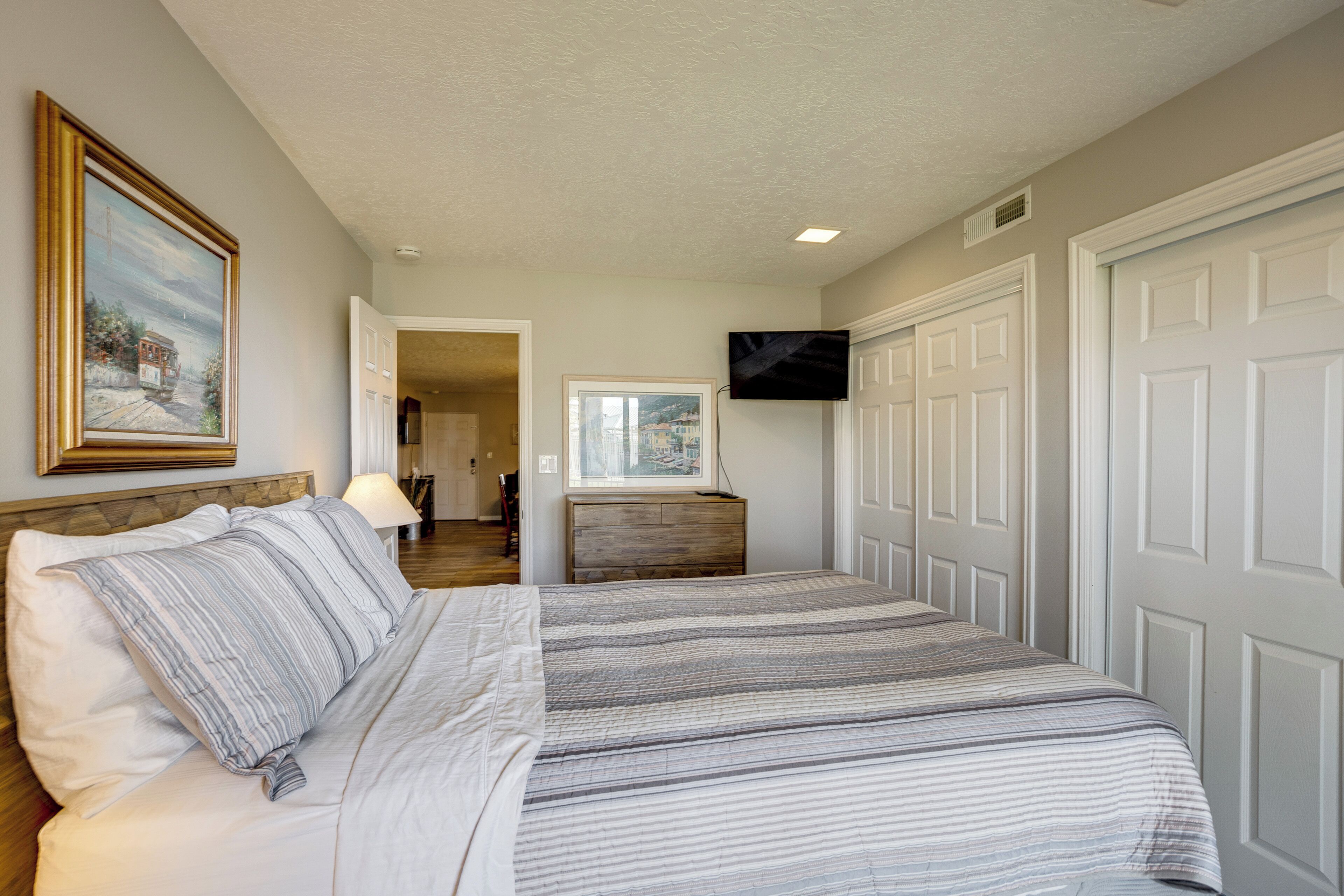 A bedroom with a bed, a TV mounted on the wall, and a door leading to another room.