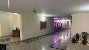 A hotel corridor with a polished floor, a wooden cabinet, a framed picture, and a planter with plants. - Spacious 3-bedroom apartment in Copacabana, 3 blocks from the beach. (Rio de Janeiro)