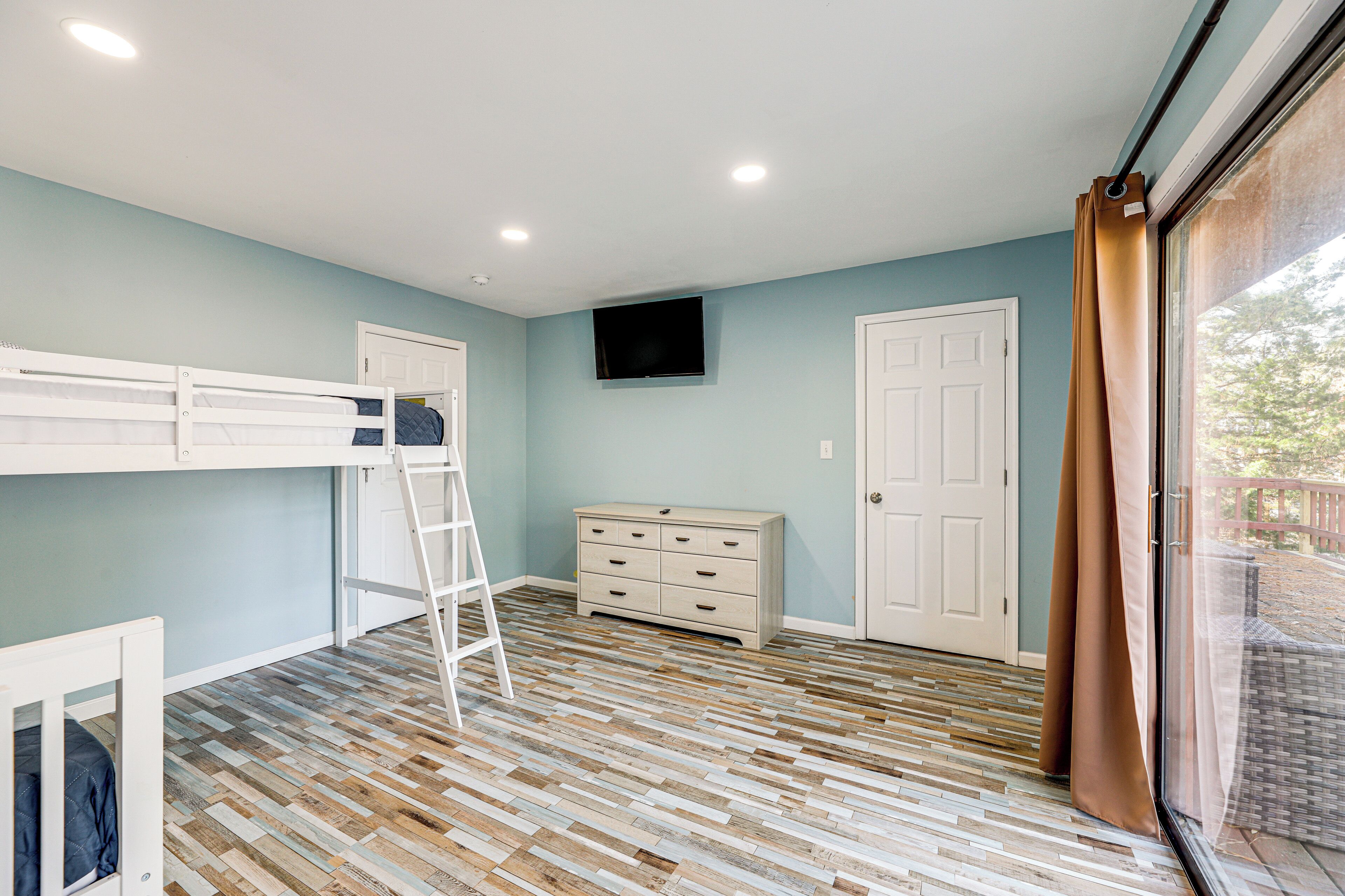 A room with a bunk bed, a dresser, a television, and a window with curtains.