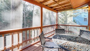 Eine überdachte Terrasse im Freien mit Holzwertung, einem Tisch mit Stühlen und Blick auf Bäume und ein Haus.