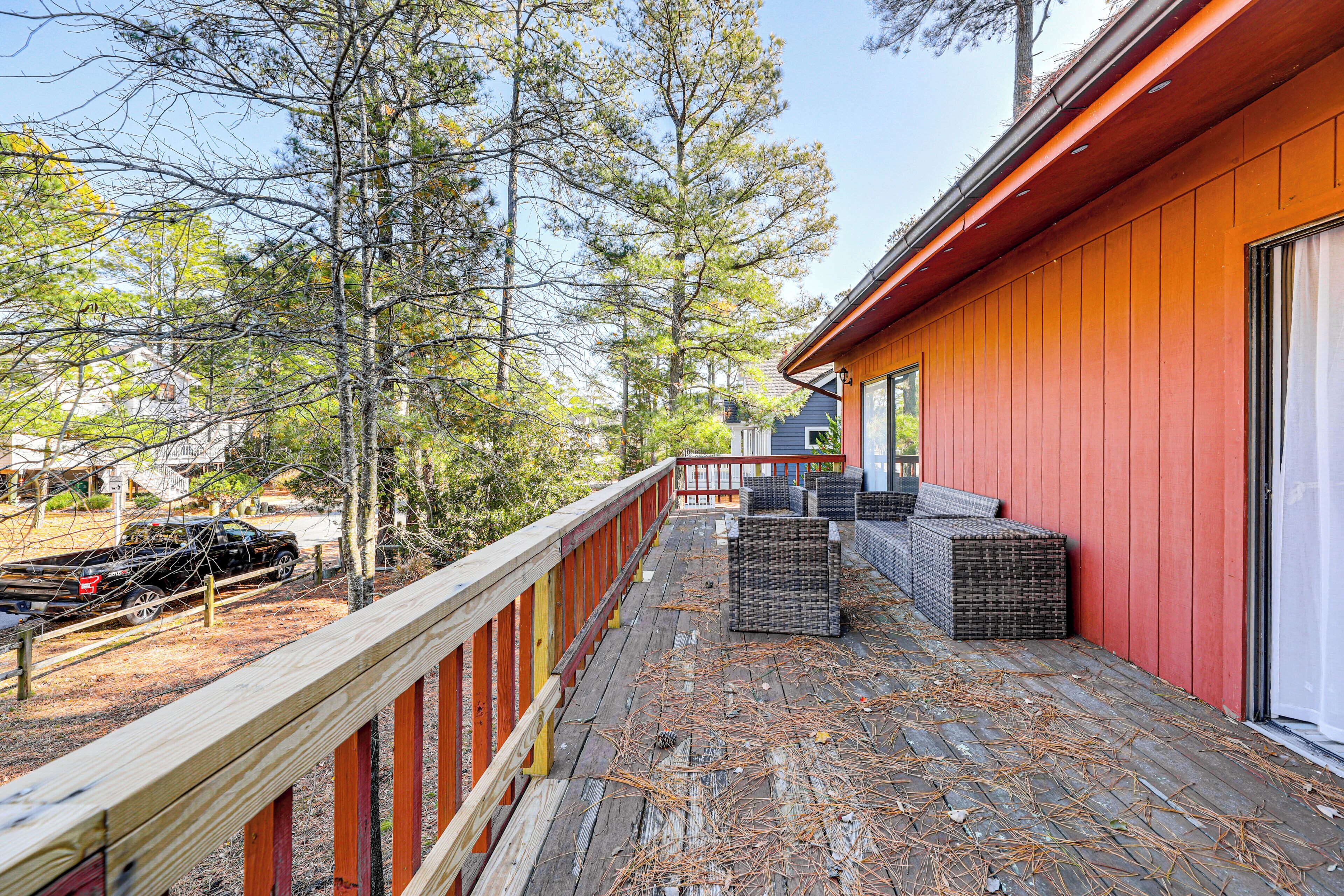 A wooden deck with a red railing, surrounded by trees and a parked truck.