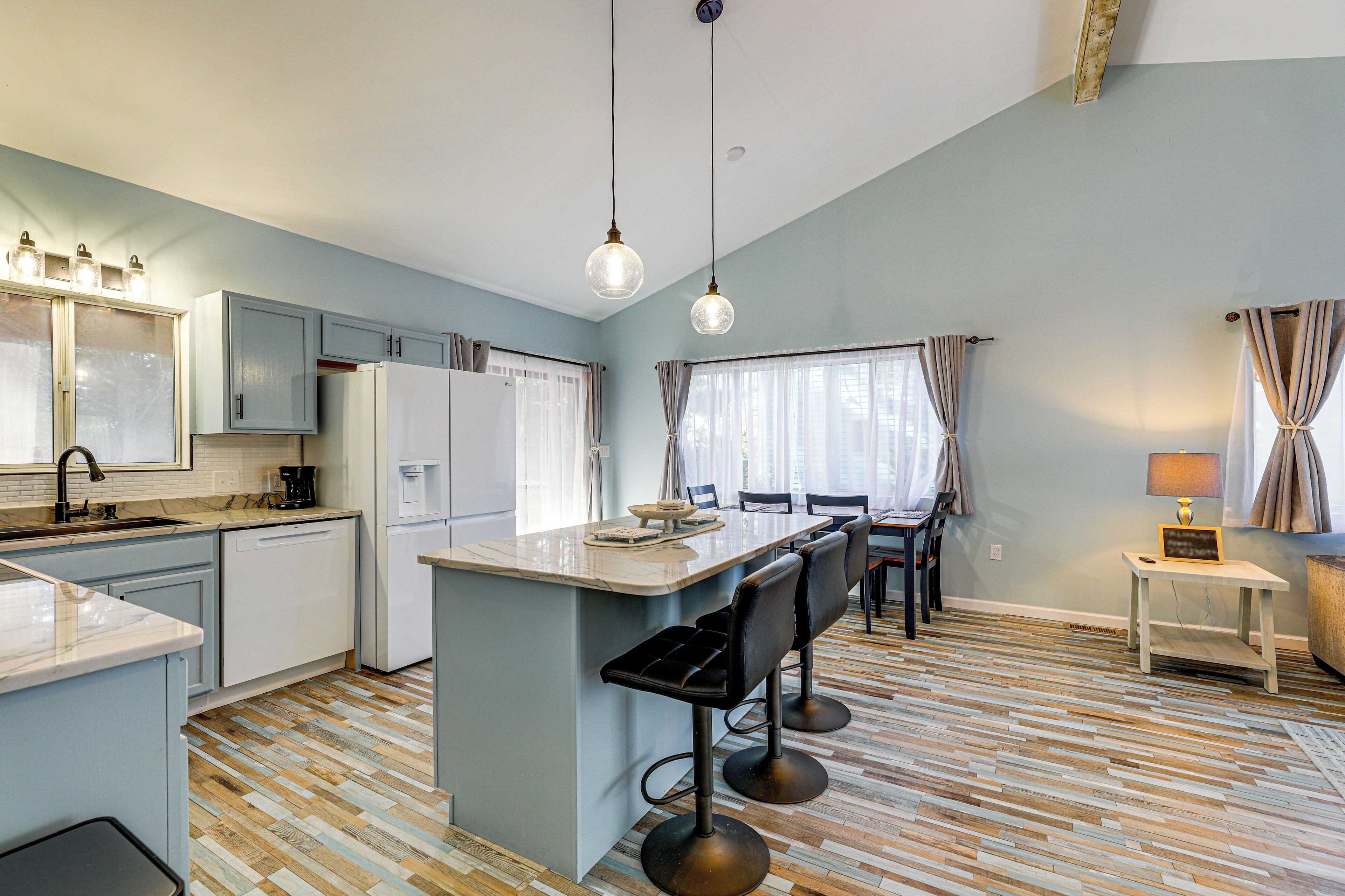 A modern kitchen with a central island, bar stools, and a dining area with a table and chairs.