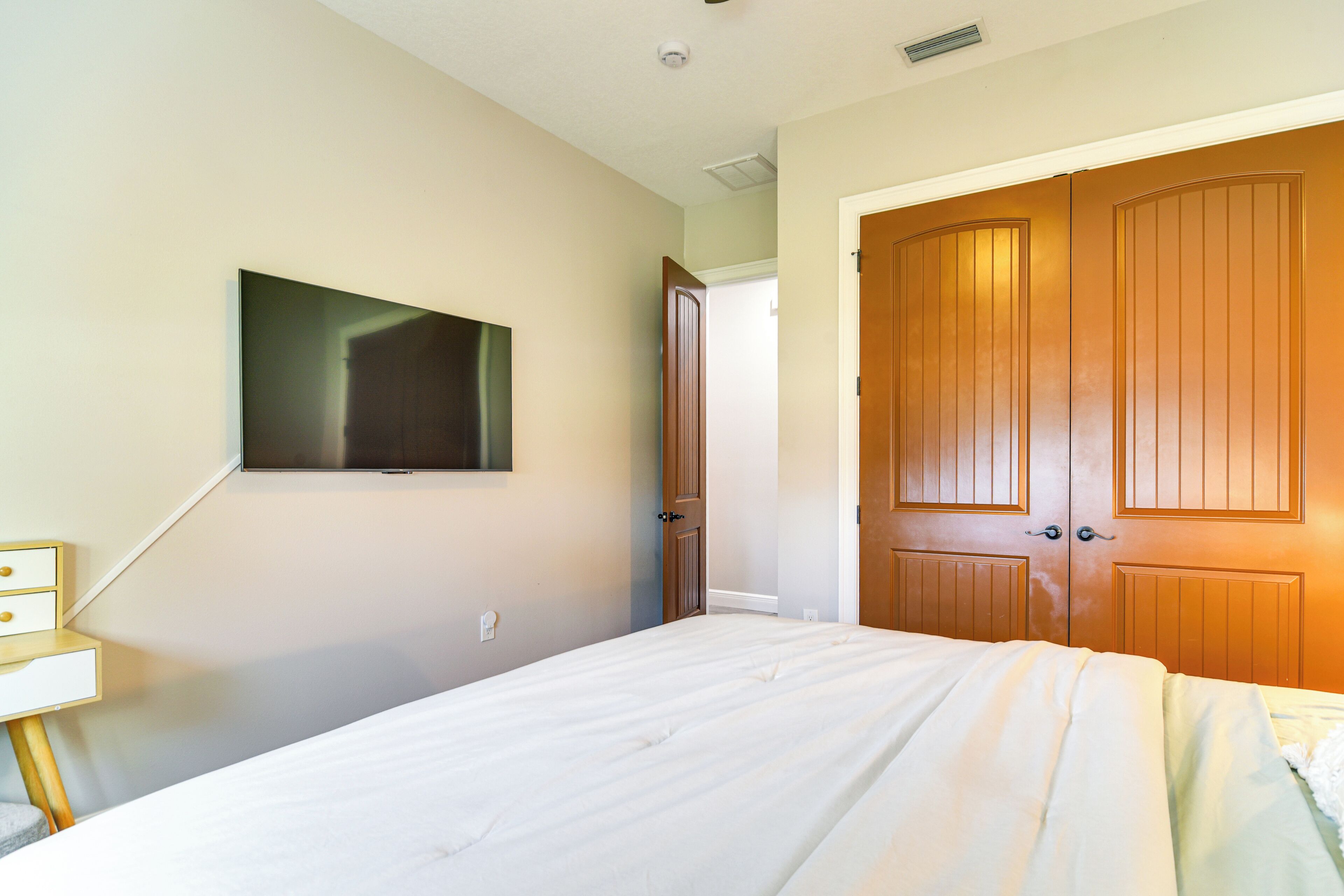 A bedroom with a bed, a TV mounted on the wall, and a wooden wardrobe.