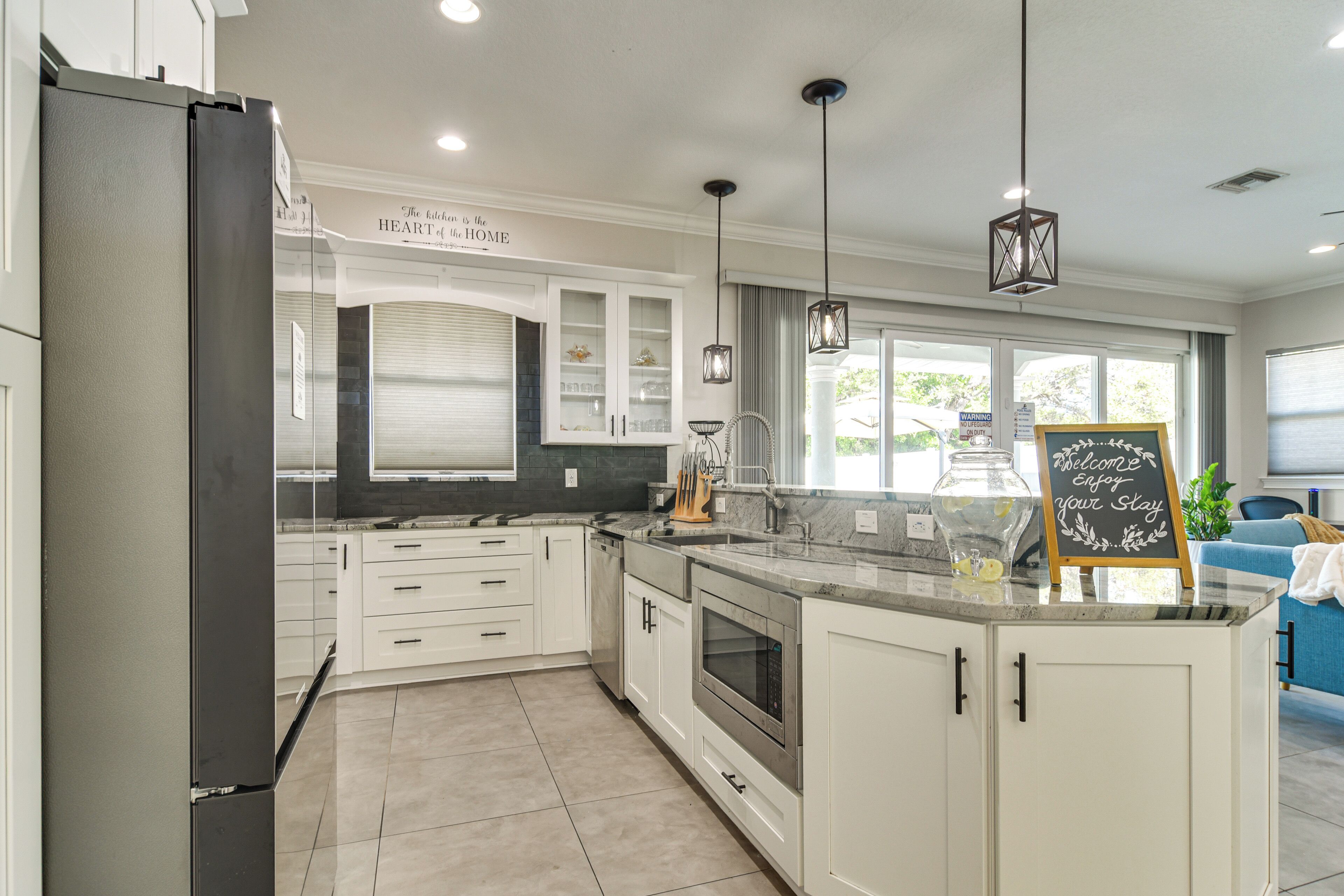 A modern kitchen with white cabinets, a built-in oven, and a large island with a chalkboard sign.
