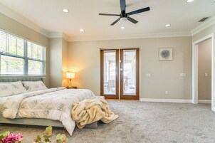 Quarto com cama, ventilador de teto, porta com vista e janela com persianas.