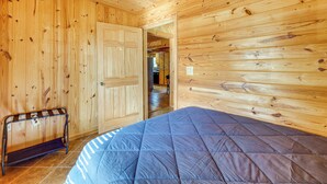 Una habitación con paneles de madera, una cama, un banco y una puerta que da a otra habitación.