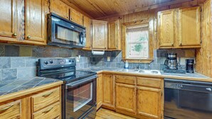 Una cocina con armarios de madera, microondas, estufa, horno, lavavajillas y una ventana con vistas.