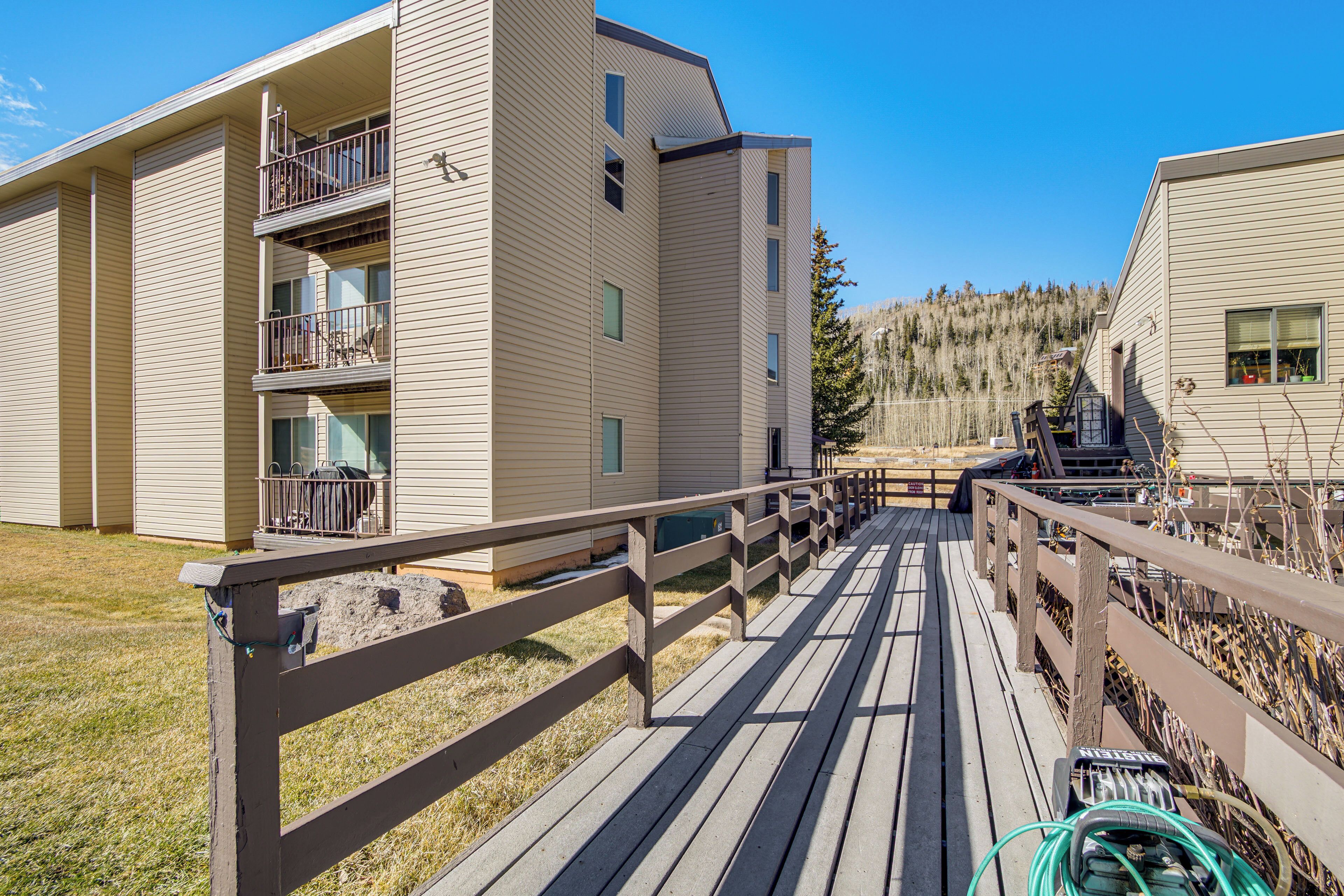Un immeuble à plusieurs étages doté de balcons, d’une terrasse en bois et offrant une vue sur une zone boisée.