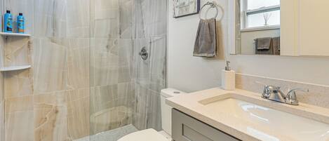 A bathroom with a shower, toilet, sink, and marble tiles.