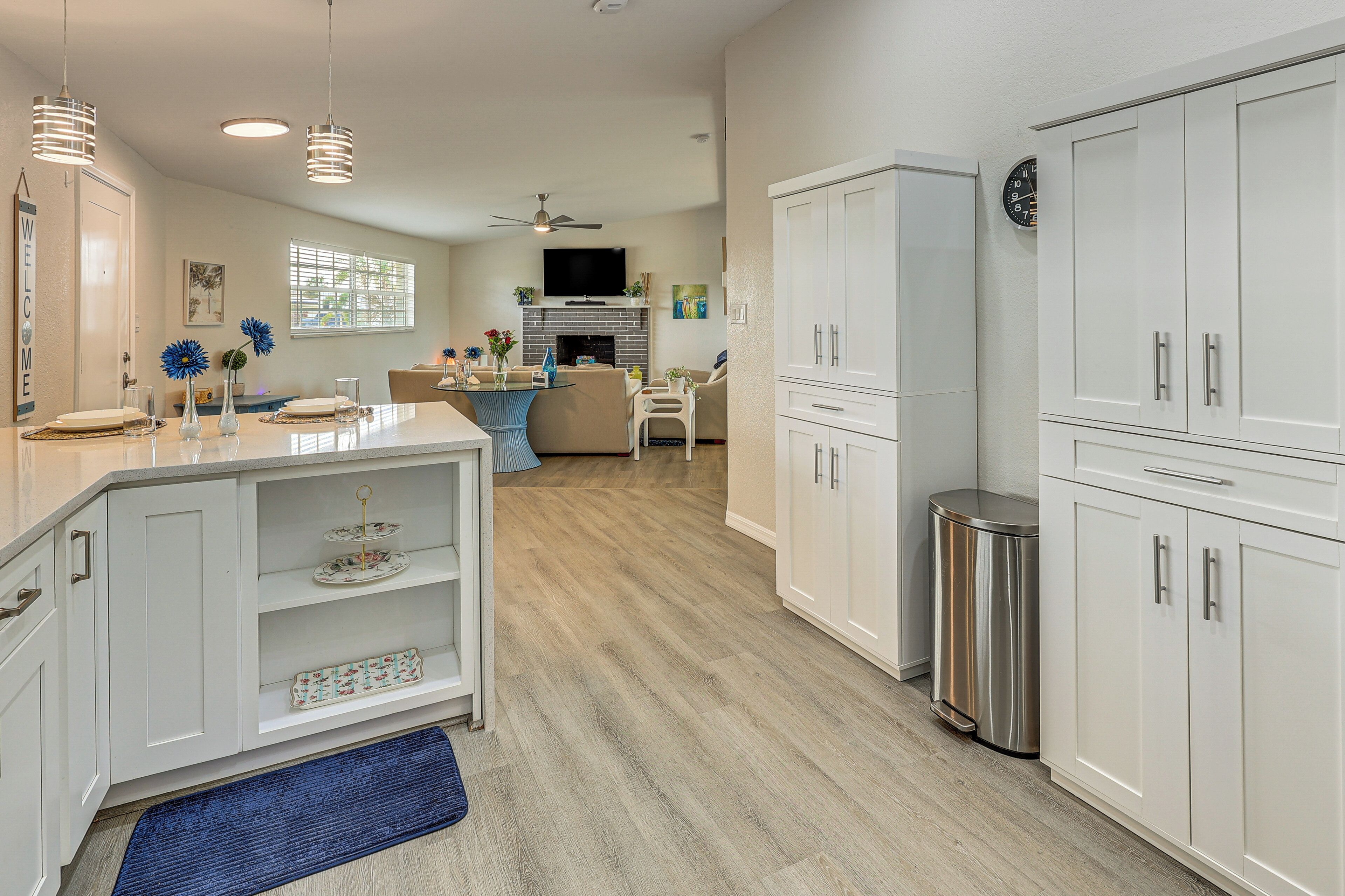 A modern kitchen with white cabinetry, a stainless steel trash can, and a dining area with a blue rug.