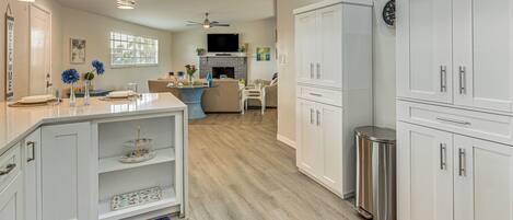 A modern kitchen with white cabinetry, a stainless steel trash can, and a dining area with a blue rug.