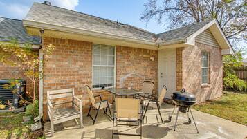 A brick house with a patio, a table, chairs, and a grill.