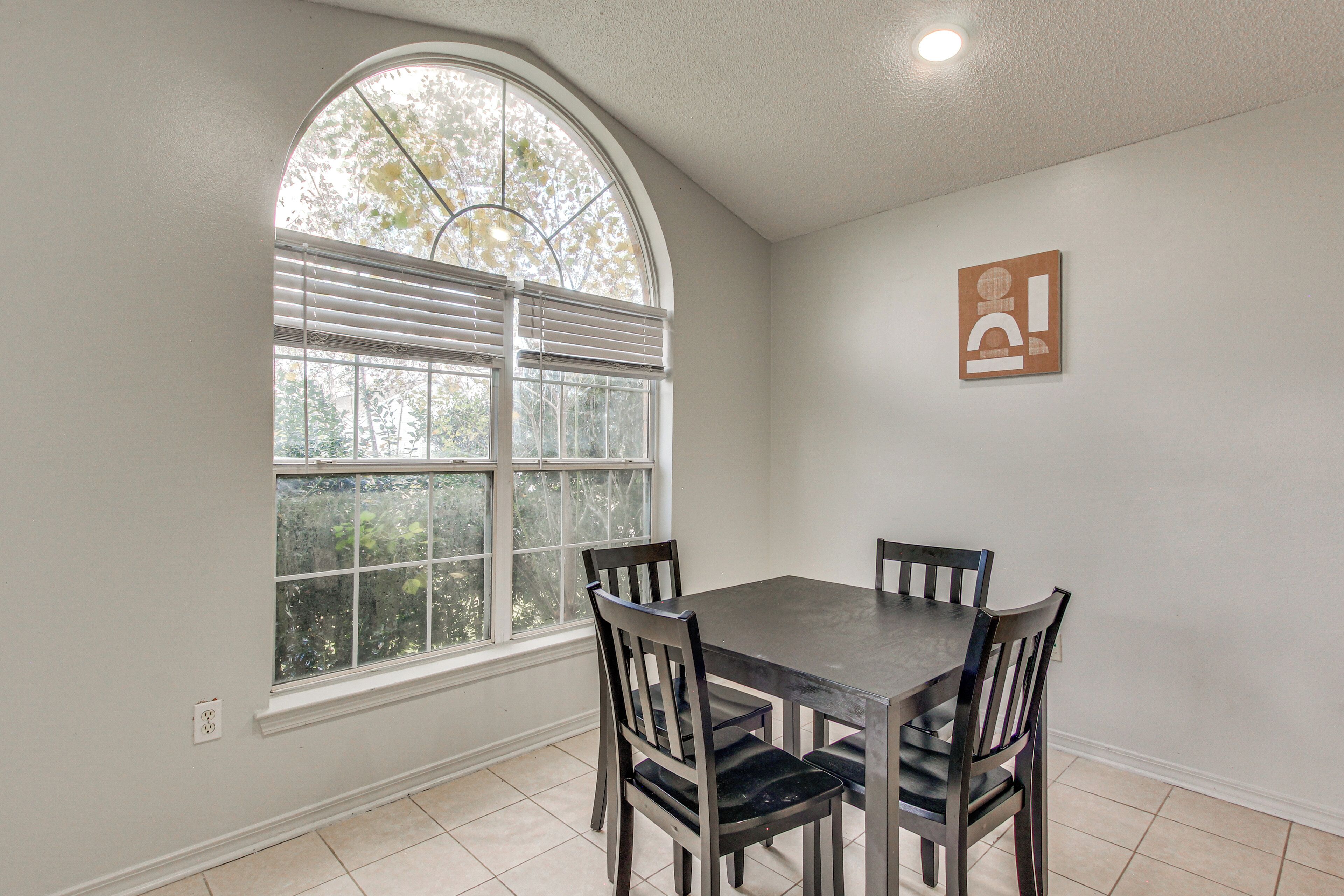 A dining area with a table and four chairs, a large arched window, and a wall-mounted light fixture.
