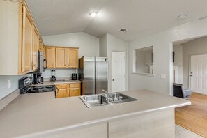 A kitchen with wooden cabinets, a stainless steel refrigerator, a double sink, and a stove. - Explore Gulfport Beaches: Family Home w/ Yard (Gulfport)