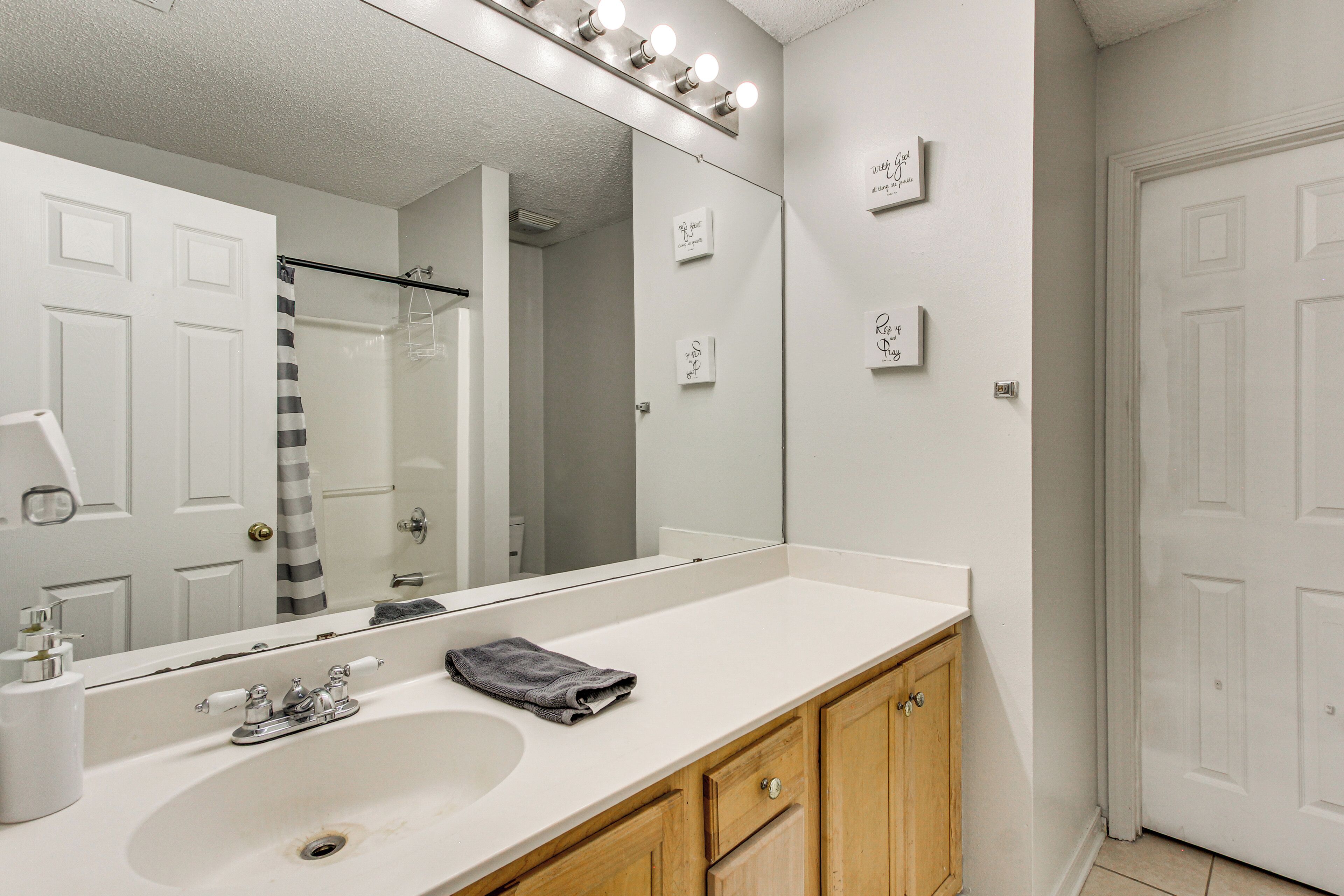 A bathroom with a large mirror, a sink, wooden cabinets, and a shower area.