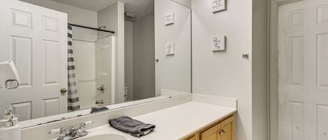 A bathroom with a large mirror, a sink, wooden cabinets, and a shower area.