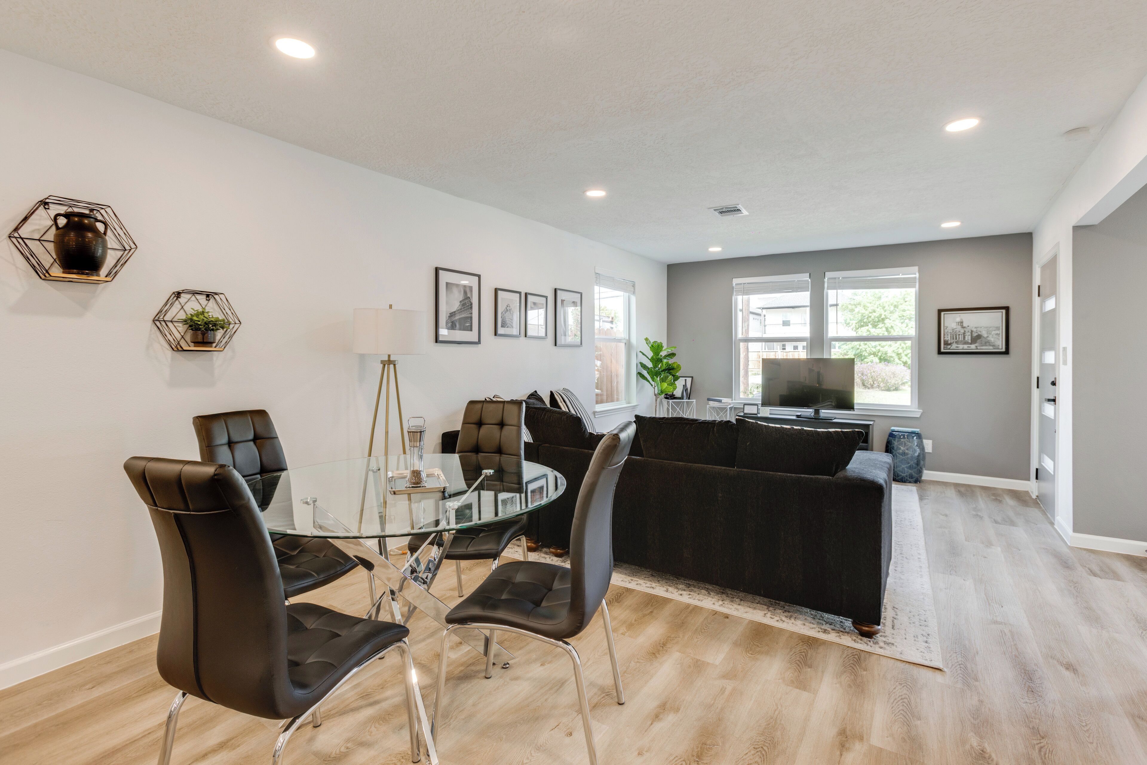 A modern living room with a glass dining table, black leather chairs, a dark sofa, and a TV.
