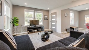 A modern living room with a large flat-screen TV, grey sofas, a coffee table, and a potted plant. - Updated Home w/ Hot Tub in Houston's Northside! (Houston)