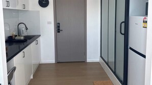 A modern kitchen with white cabinets, a black countertop, a clock, and a door leading to a glass-enclosed area. - Metawise Peaceful Home Close to Monash Uni and Chadstone U2 (Melbourne)