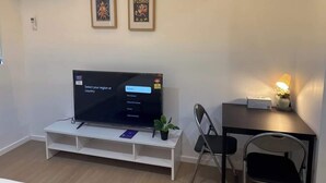 A modern living room with a flat-screen TV on a white stand, two framed pictures on the wall, a small table with a lamp, and a chair. - Metawise Peaceful Home Close to Monash Uni and Chadstone U2 (Melbourne)