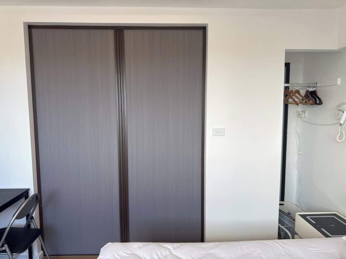 A hotel room with a large sliding door closet, a bed, a desk, and a small bathroom area with a shower.