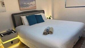 A neatly made bed with white bedding and two blue pillows, a bedside table with a lamp, and a framed picture on the wall. - Metawise Peaceful Home Close to Monash Uni and Chadstone U2 (Melbourne)