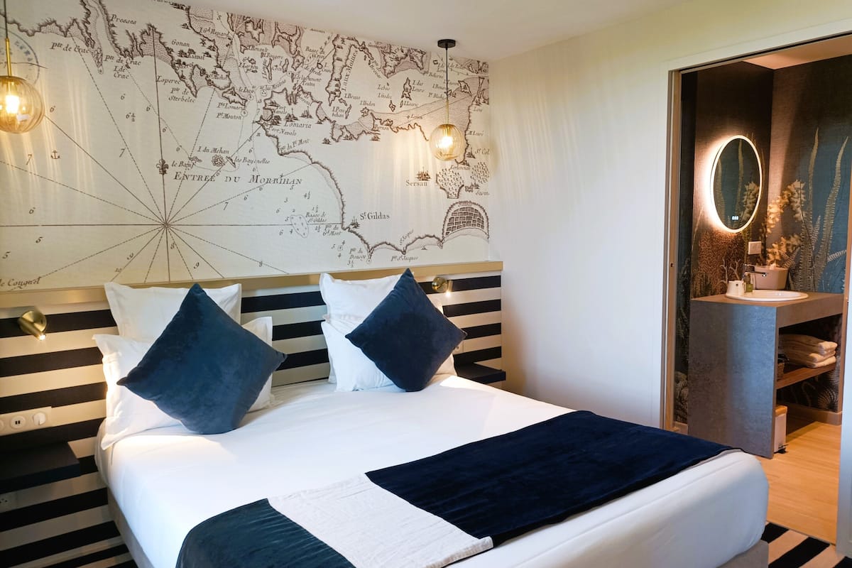 Habitación de hotel con una cama grande, un mapa en la pared, un baño moderno y un suelo a rayas.