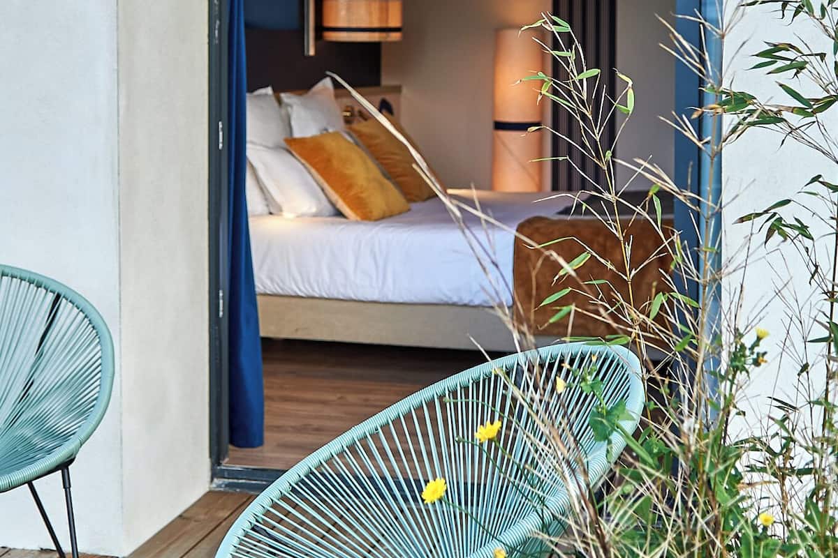 Un dormitorio moderno con una cama, dos sillas y una terraza de madera.