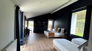 A modern, well-lit room with a wooden floor, a sofa, a bed, and a dining area with a table and chairs. - Hôtel de La Marine (Groix)