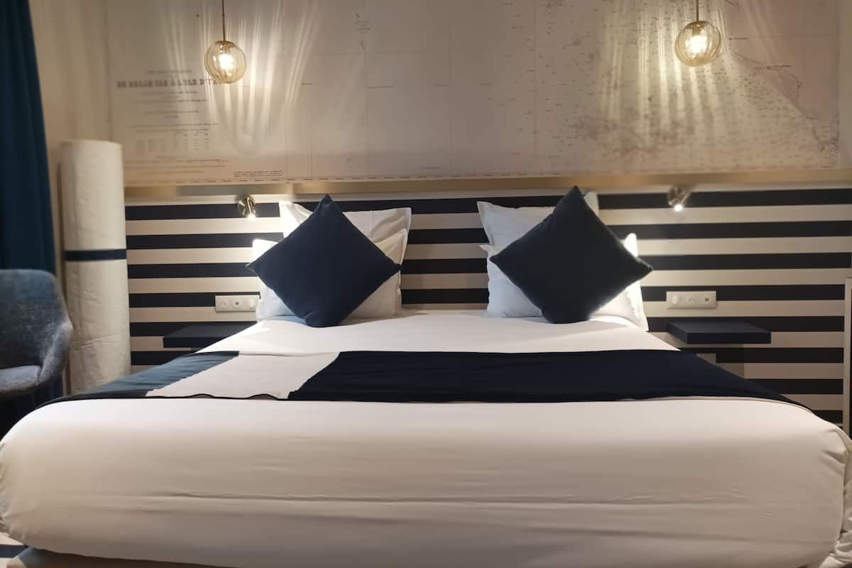 Habitación de hotel con una cama grande, dos cabeceros a rayas blancas y negras y dos lámparas colgantes.