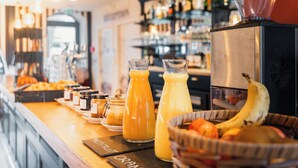 A breakfast bar with orange juice, a fruit basket, and a coffee machine. - Hôtel de La Marine (Groix)