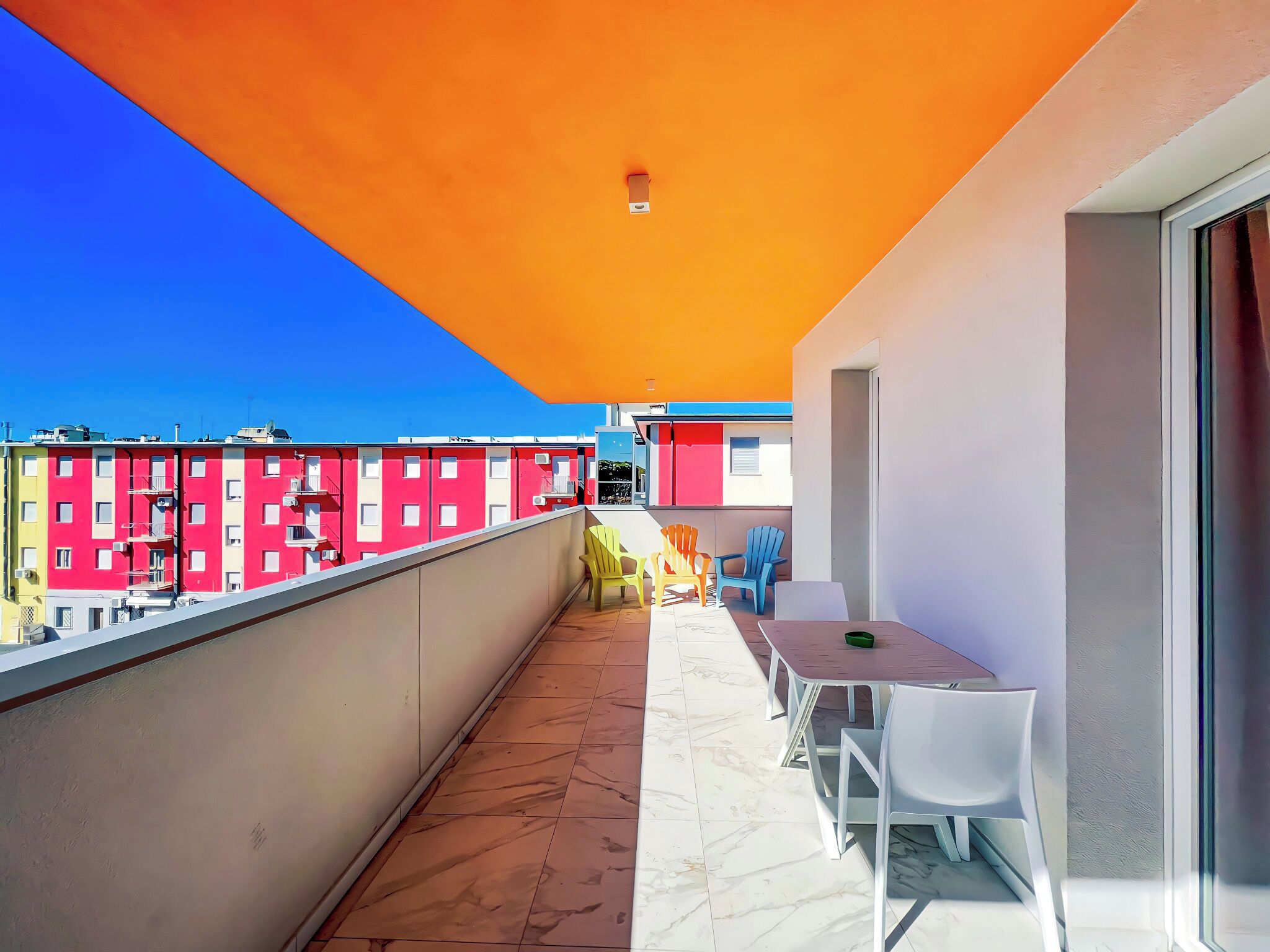 Un balcon doté d’un sol carrelé, d’une table avec des chaises, et offrant une vue sur des bâtiments aux couleurs vives en arrière-plan.