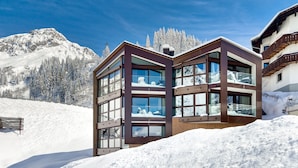A modern multi-story building with large windows, set against a snowy mountain backdrop.