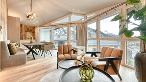 A modern living room with a dining area, large windows, and a view of mountains.