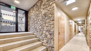 A hotel corridor with stone walls, wooden doors, and a tiled floor.
