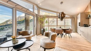 Un salón amplio con una gran mesa de comedor, asientos cómodos y vistas a las montañas a través de ventanas panorámicas.