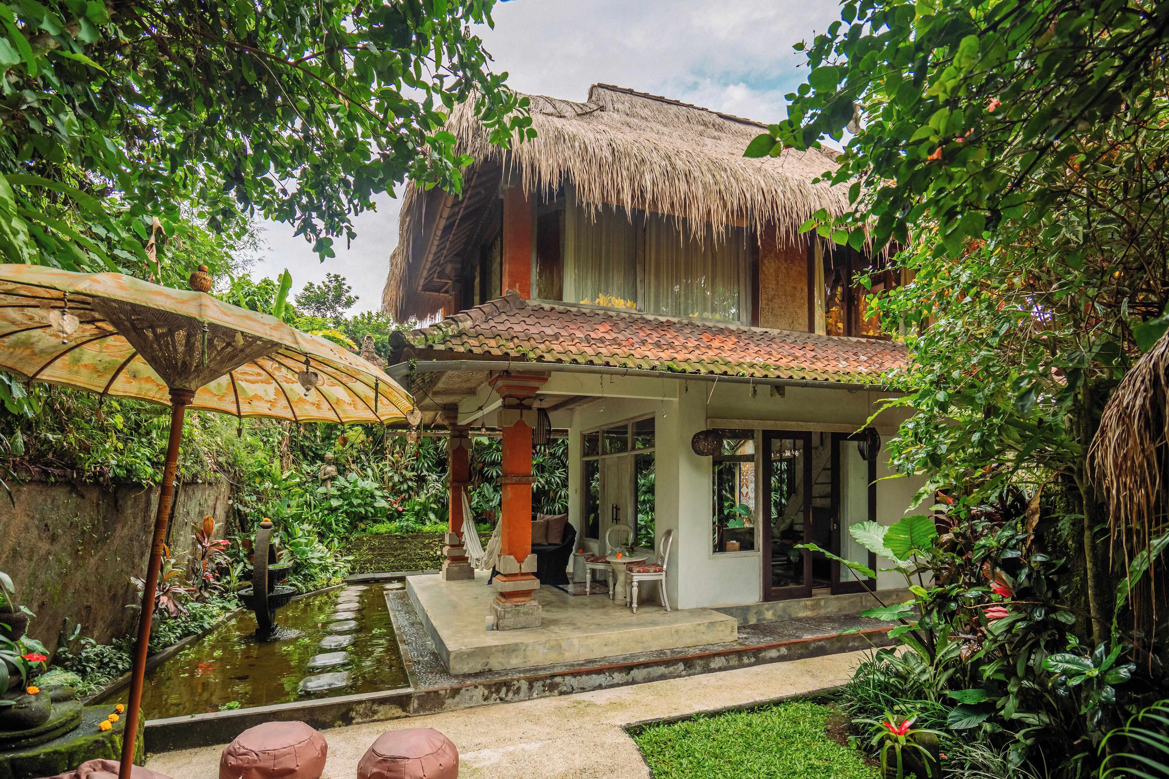 A traditional house with a thatched roof, a small pond, and a covered seating area with a table and chairs.