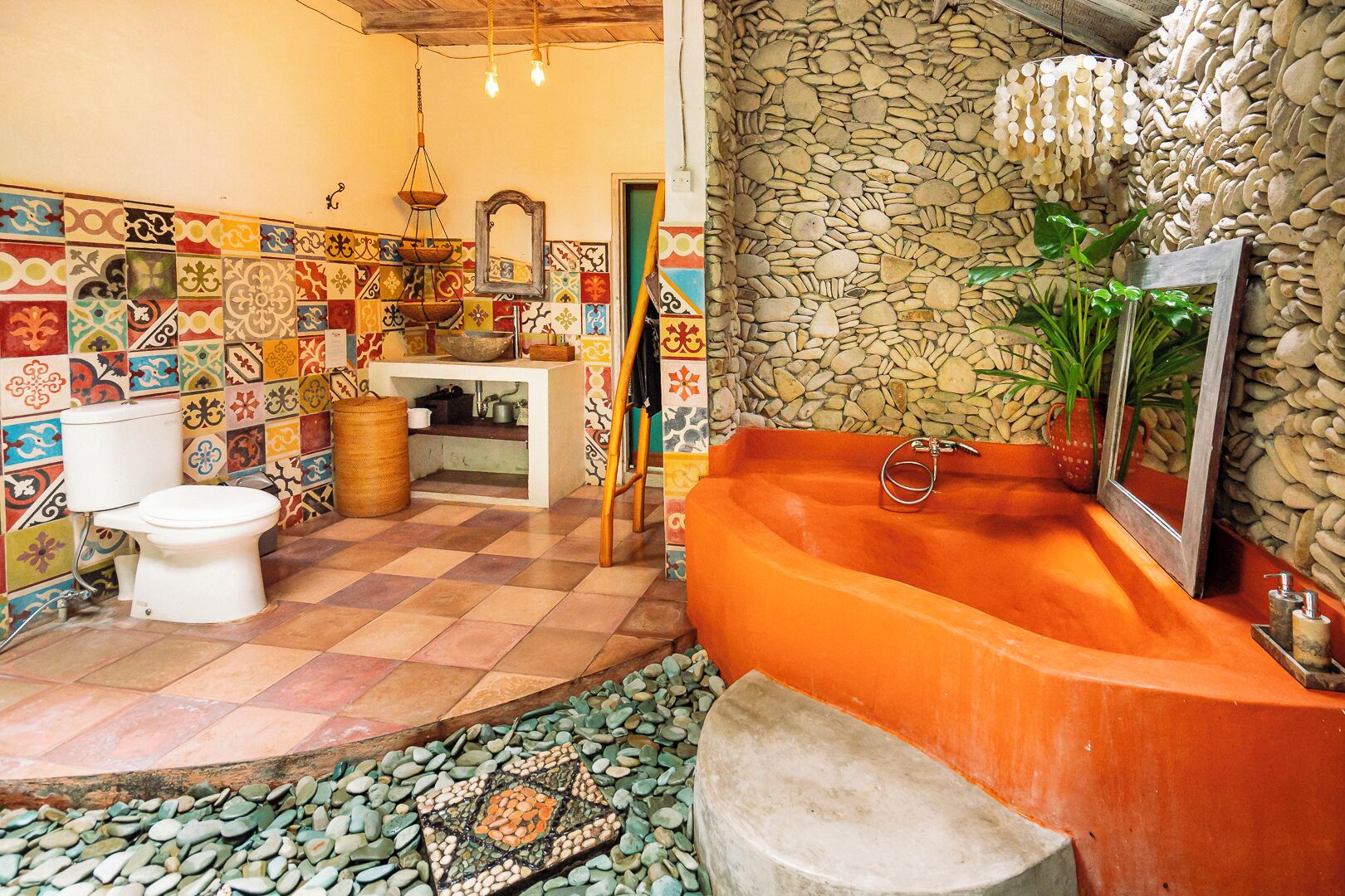 A bathroom with a checkered floor, a white toilet, a sink with a mirror, and a bathtub with a stone wall.